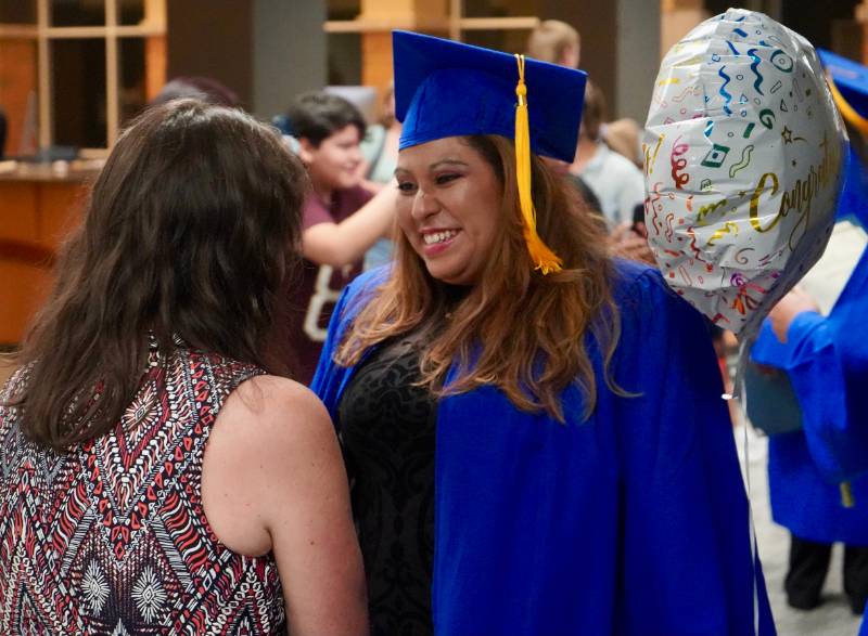 A woman graduate shakes hands while be congratulated by an excited family member