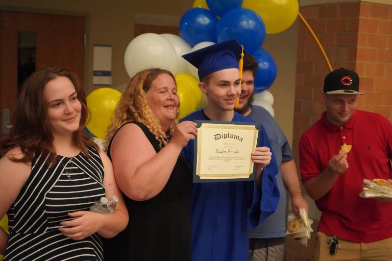 A young ABE graduate shows off his diploma surrounded by family