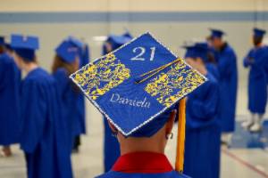 An ABE graduate shows off their decorated graduation cap. It is decorated in gold with the number 21 and their name.