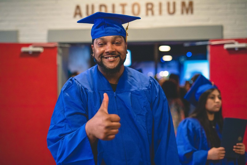 An ABE graduate gives the thumbs up sign in his cap and gown at graduation.