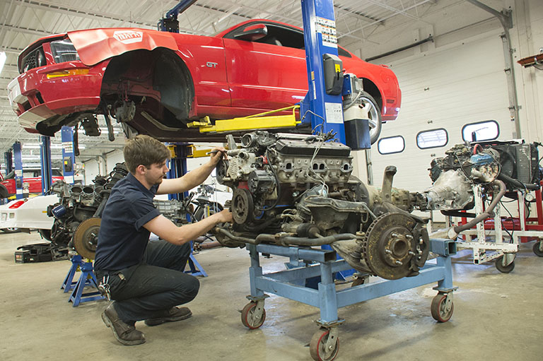 An automotive technology major working on the engine of a red vehicle