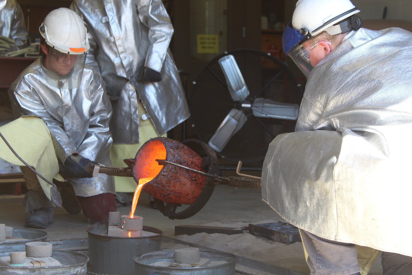 VU students and instructor practice pouring molten metal into a form for casting