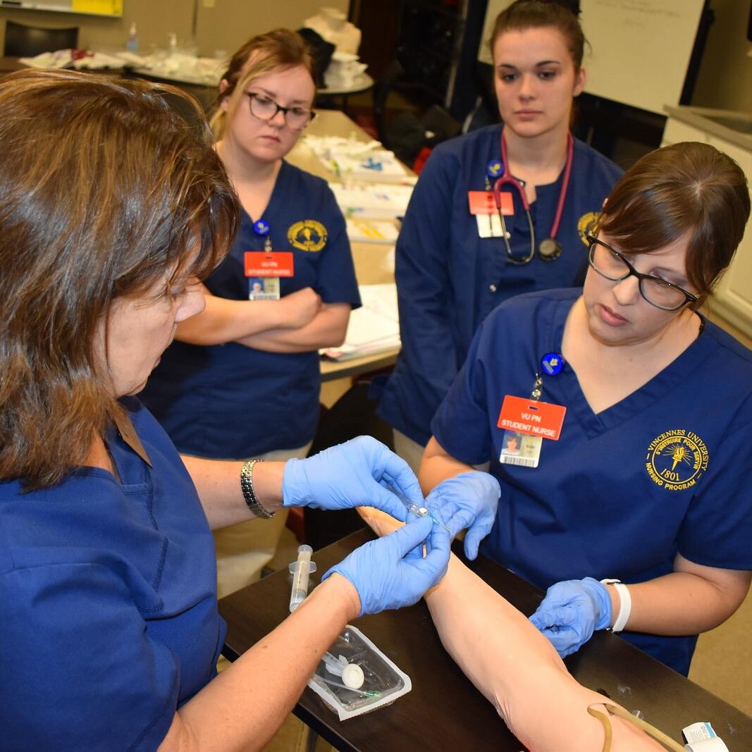 A group of nursing students using needles on a training arm