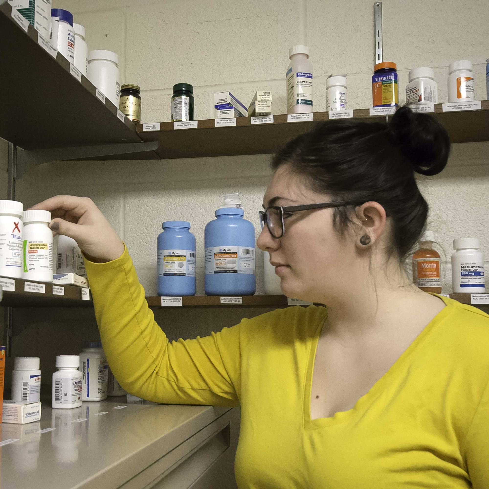 Young woman picking up a medicine bottle off of a shelf