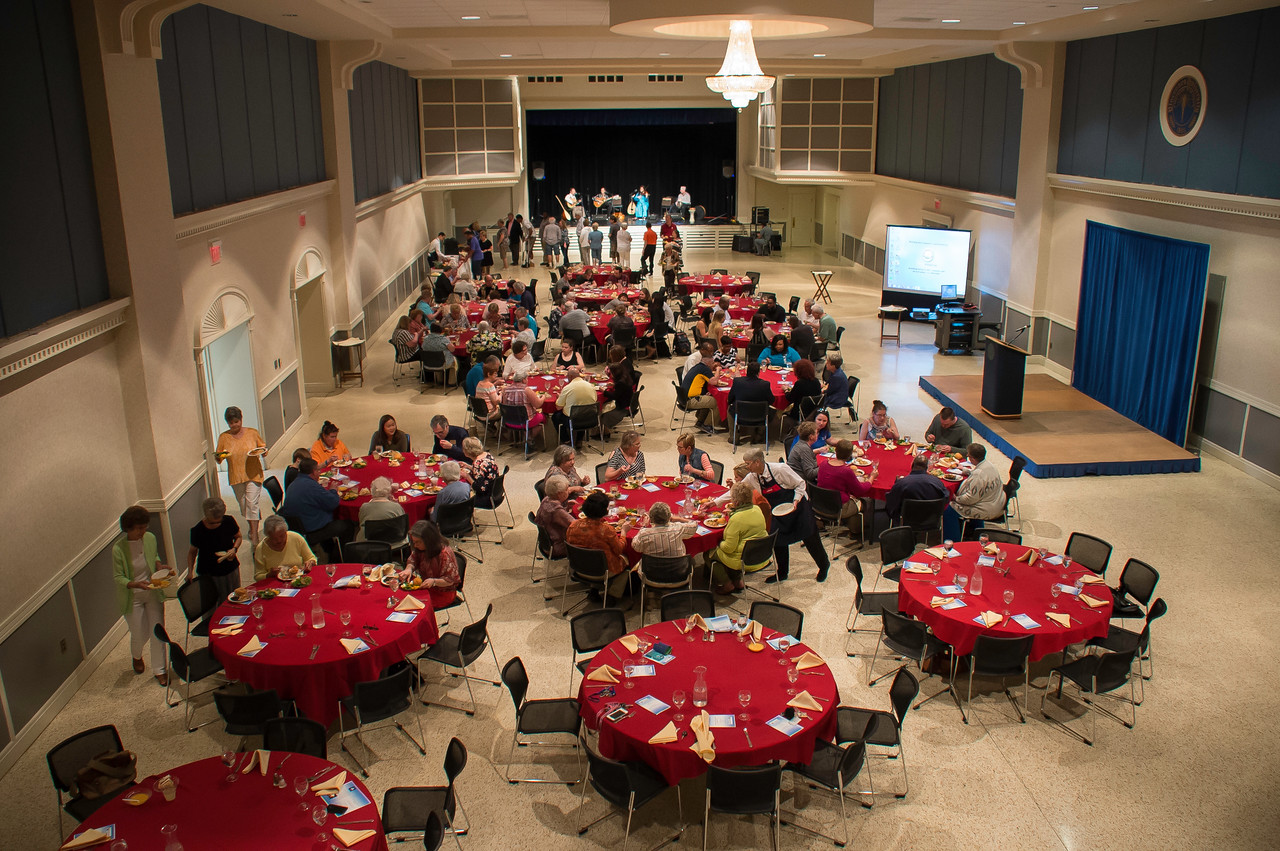 A large group of older individuals in a large room sitting at red circular tables