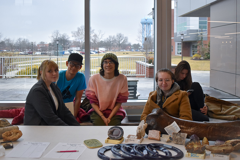 A group of four students sit by a large window displaying fossils and artifacts on a table.