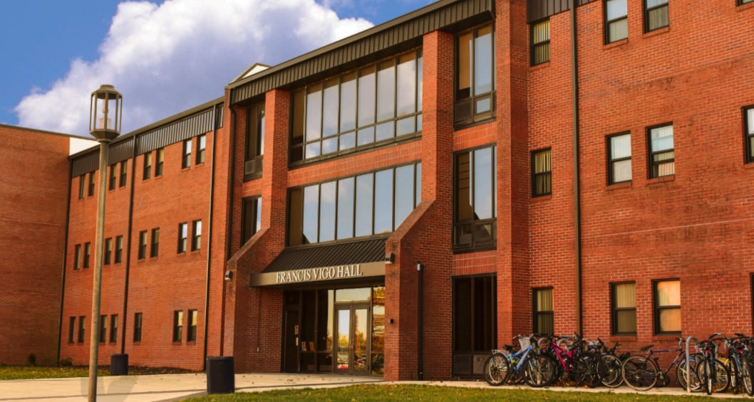 The entrance to Vigo hall is shown with the reflections of white clouds in a bright blue sky, bicycles stand in line next to the entrance.
