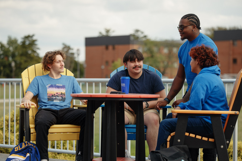 Students sitting at a table in a group outside engaging in conversation.
