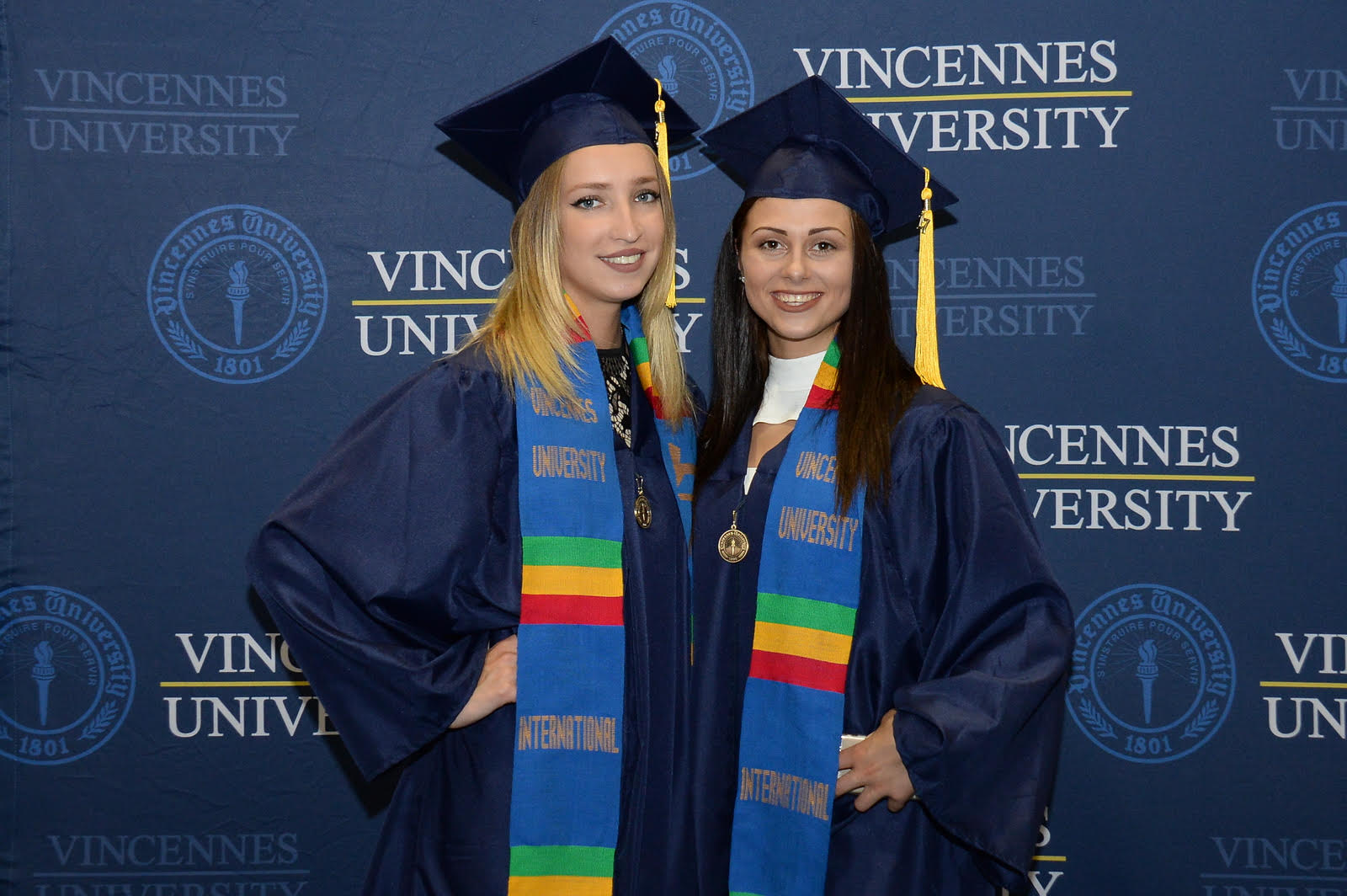 Two young ladies one blonde and one brunette smile for the photographer at graduation
