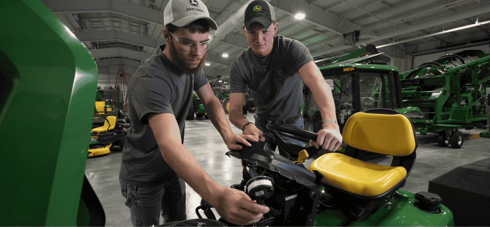Two students working on the engine of a John Deere lawn tractor.